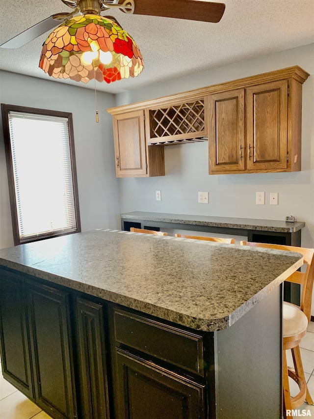 kitchen featuring a kitchen breakfast bar, a textured ceiling, a center island, and a ceiling fan