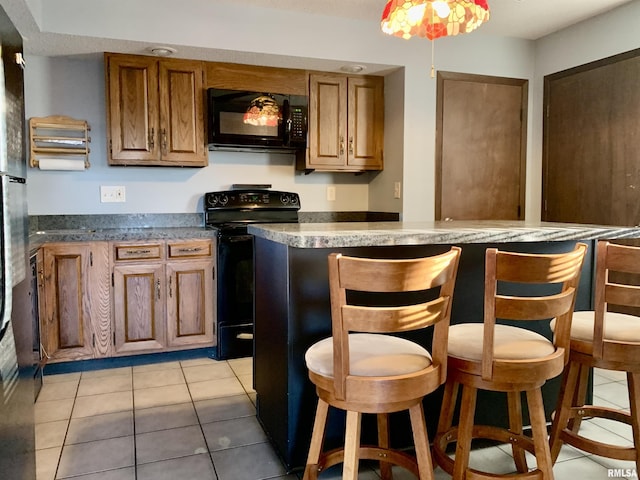 kitchen with light tile patterned floors, a breakfast bar area, black appliances, and brown cabinets