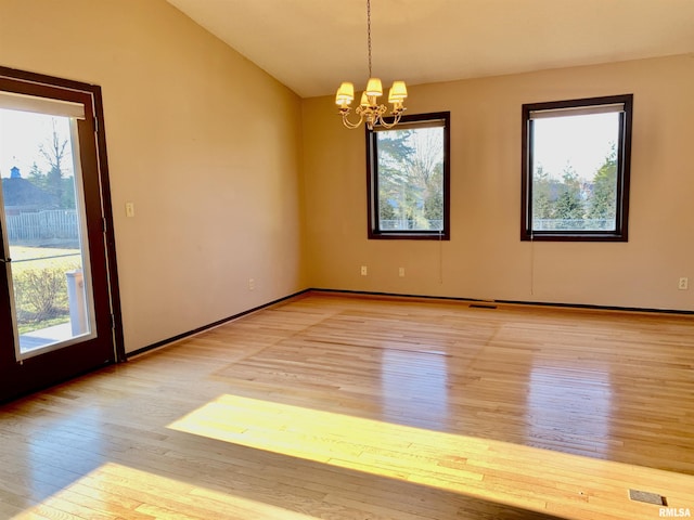 unfurnished room featuring a wealth of natural light, lofted ceiling, light wood-type flooring, and an inviting chandelier