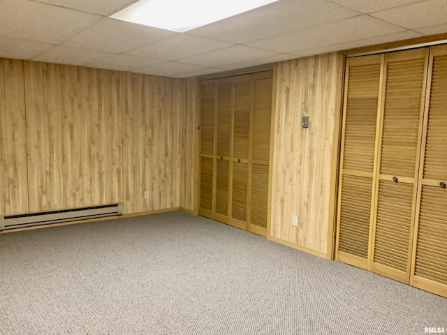 interior space featuring carpet flooring, a paneled ceiling, wood walls, and baseboard heating