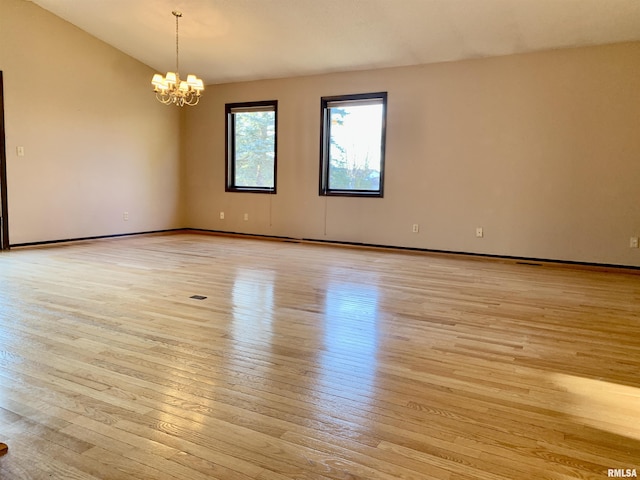 empty room featuring a chandelier, light wood-type flooring, and vaulted ceiling