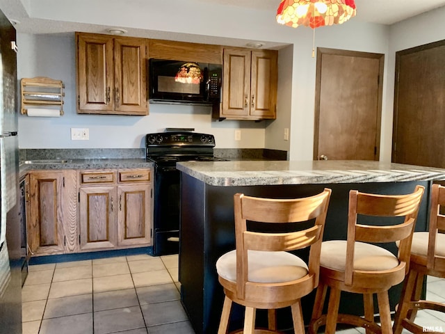 kitchen featuring a kitchen bar, black appliances, light tile patterned flooring, and brown cabinets