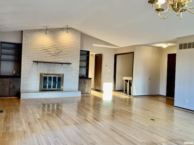 unfurnished living room with wood finished floors, visible vents, an inviting chandelier, a fireplace, and vaulted ceiling