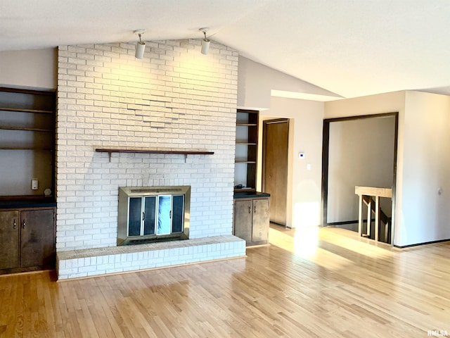 unfurnished living room with vaulted ceiling, a fireplace, baseboards, and wood finished floors