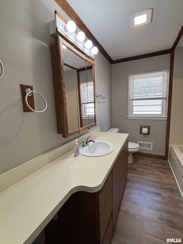 full bath with vanity, wood finished floors, visible vents, crown molding, and toilet