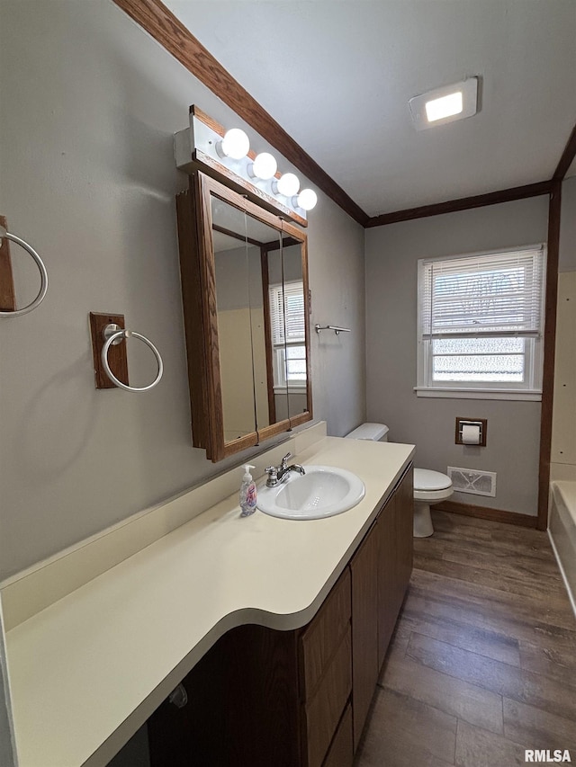 bathroom featuring visible vents, toilet, ornamental molding, wood finished floors, and vanity