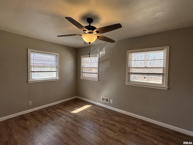 empty room featuring dark wood-type flooring, a ceiling fan, baseboards, and visible vents