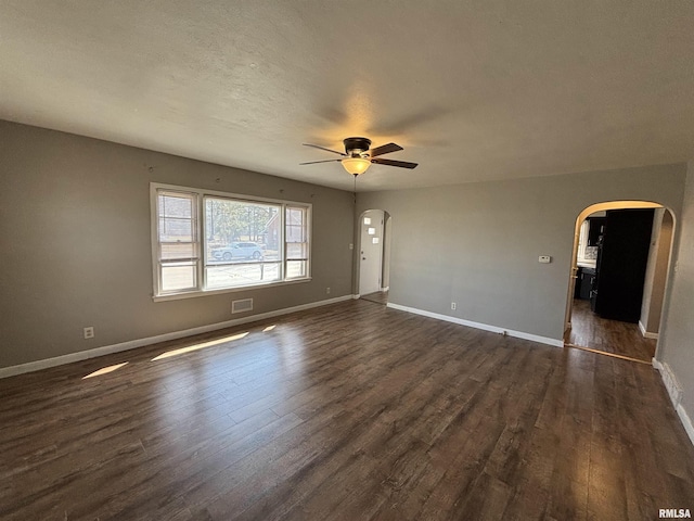 spare room with dark wood finished floors, baseboards, arched walkways, and ceiling fan