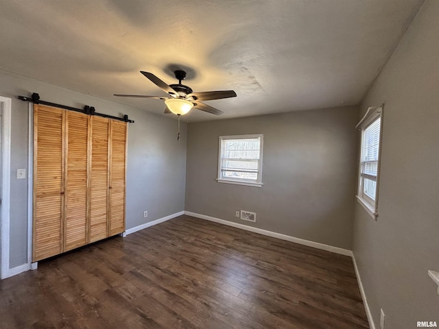 unfurnished bedroom with a barn door, baseboards, and dark wood-type flooring