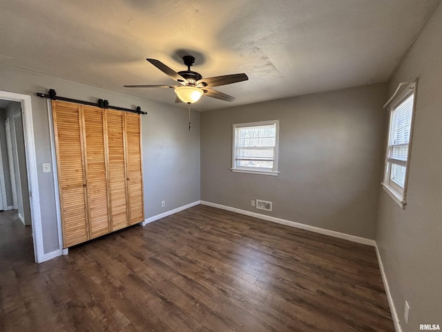 unfurnished bedroom featuring a barn door, baseboards, visible vents, and dark wood-style flooring