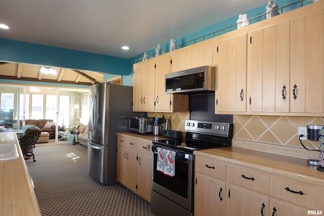 kitchen featuring light brown cabinets, open floor plan, light colored carpet, decorative backsplash, and stainless steel appliances