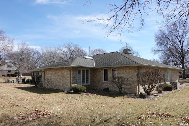 back of property featuring a yard, brick siding, roof with shingles, and a chimney