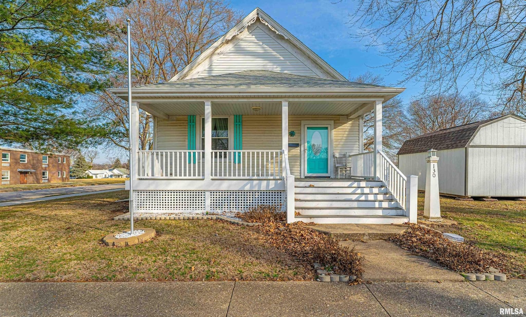 bungalow with an outbuilding, roof with shingles, covered porch, a front lawn, and a storage shed