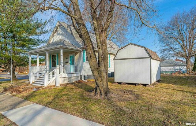 view of front of property with a front lawn, a shed, roof with shingles, covered porch, and an outdoor structure