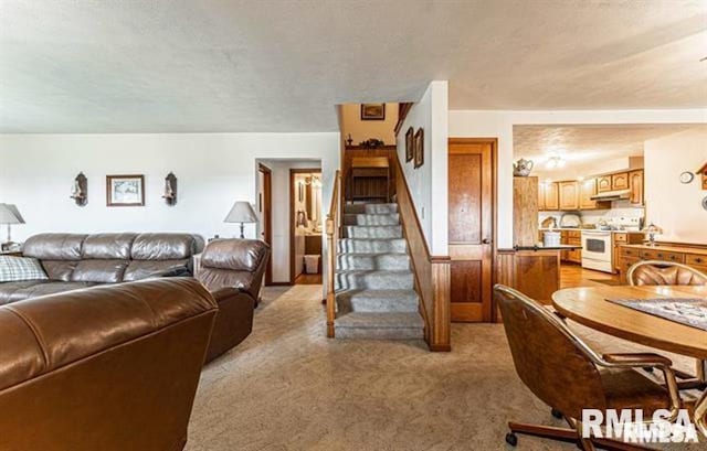 living area with stairway, light colored carpet, and a textured ceiling