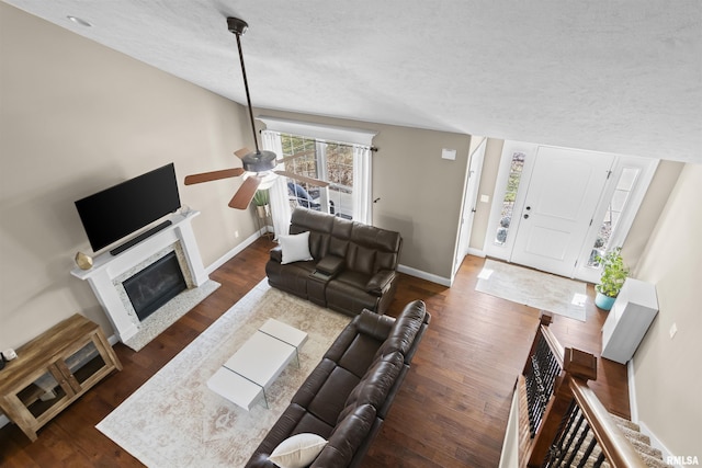 living room with ceiling fan, baseboards, wood finished floors, a glass covered fireplace, and a textured ceiling