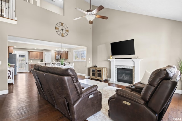 living area with a fireplace, ceiling fan with notable chandelier, baseboards, and dark wood-style flooring