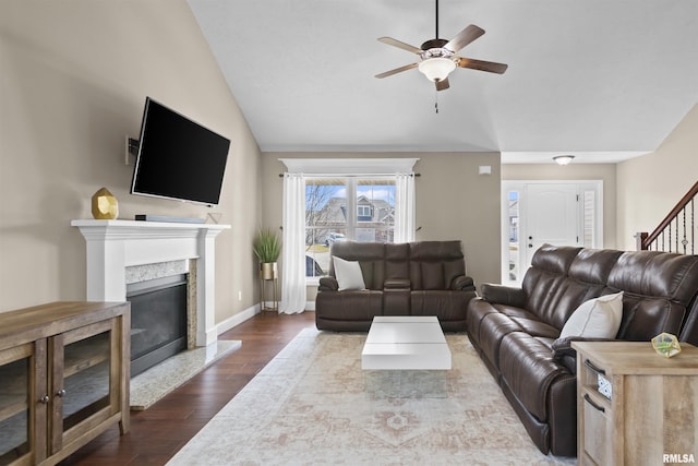 living room featuring stairway, lofted ceiling, a fireplace, ceiling fan, and dark wood-type flooring