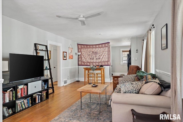 living area featuring light wood-type flooring, baseboards, visible vents, and ceiling fan