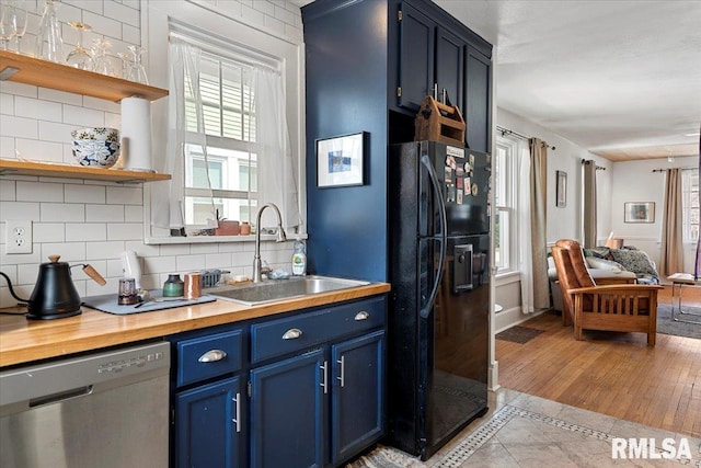 kitchen featuring blue cabinetry, a sink, dishwasher, backsplash, and black refrigerator with ice dispenser