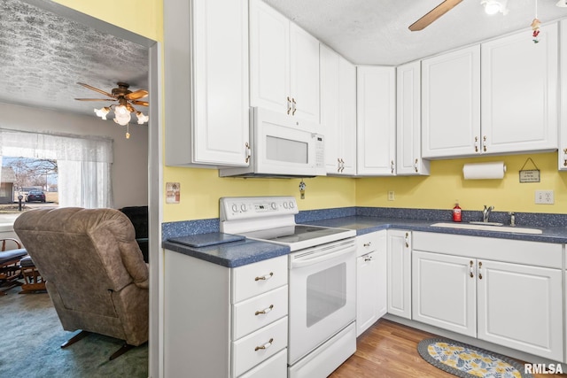 kitchen with a ceiling fan, a sink, dark countertops, white appliances, and white cabinets