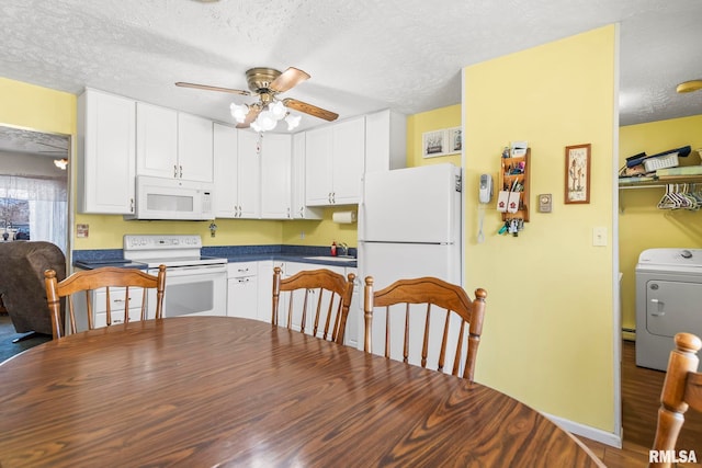 kitchen with white appliances, dark countertops, washer / dryer, and white cabinetry