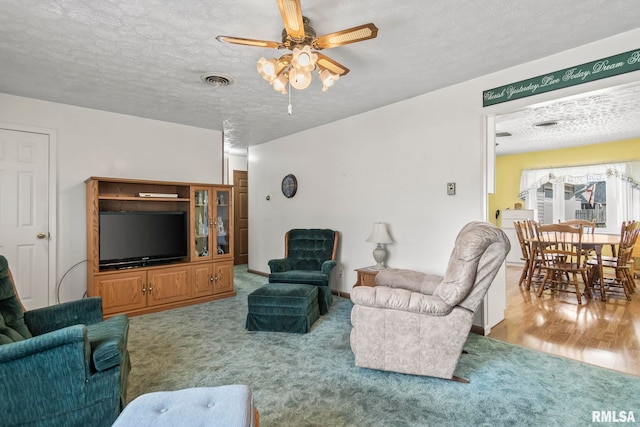 living area with visible vents, baseboards, ceiling fan, carpet floors, and a textured ceiling