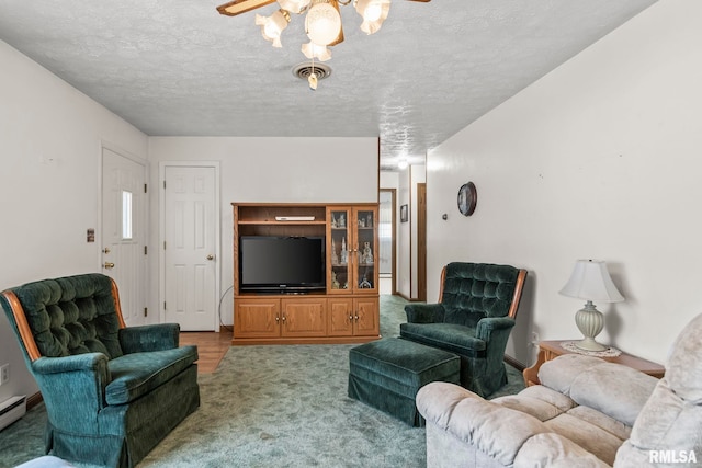 living area with a baseboard heating unit, a textured ceiling, visible vents, and carpet flooring