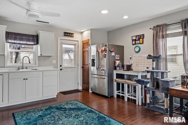 kitchen featuring dark wood-style floors, stainless steel fridge with ice dispenser, a sink, light countertops, and white cabinetry