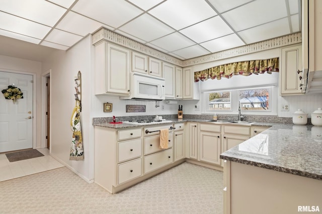 kitchen featuring white appliances, cream cabinets, a drop ceiling, and a sink