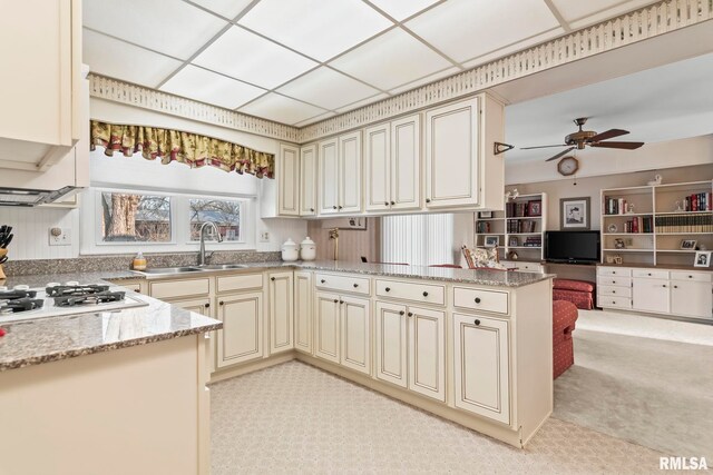 kitchen with light stone counters, a peninsula, ceiling fan, a sink, and cream cabinets