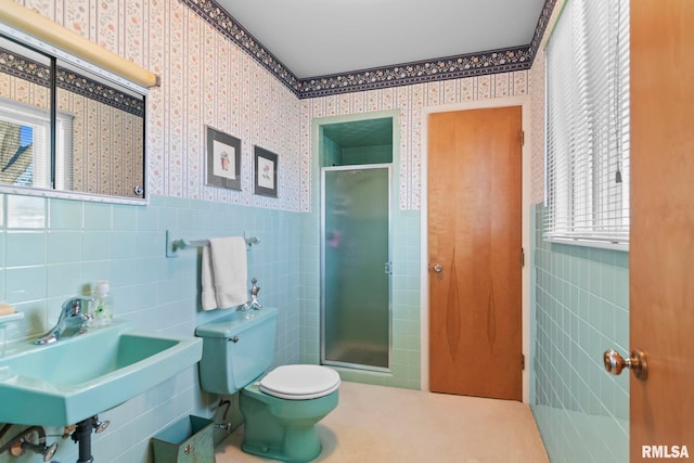 full bath with wallpapered walls, a stall shower, a sink, wainscoting, and toilet