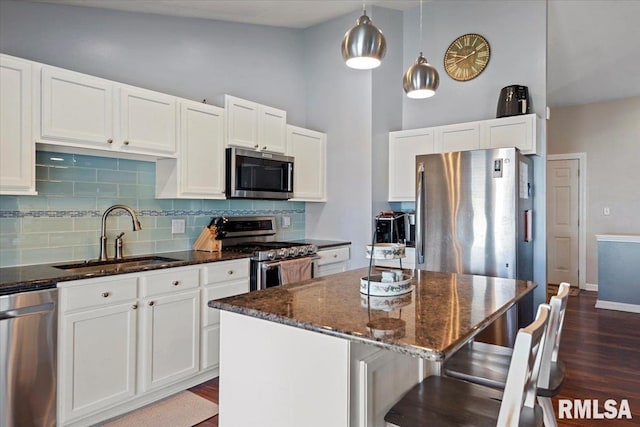 kitchen with dark stone counters, a sink, stainless steel appliances, white cabinets, and a center island