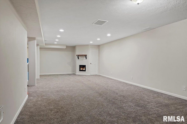 unfurnished living room featuring carpet, visible vents, a warm lit fireplace, and baseboards