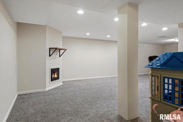 below grade area featuring a glass covered fireplace, recessed lighting, baseboards, and carpet floors