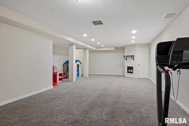 rec room with a textured ceiling, baseboards, visible vents, and a lit fireplace