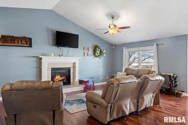 living area featuring a ceiling fan, baseboards, dark wood finished floors, vaulted ceiling, and a glass covered fireplace