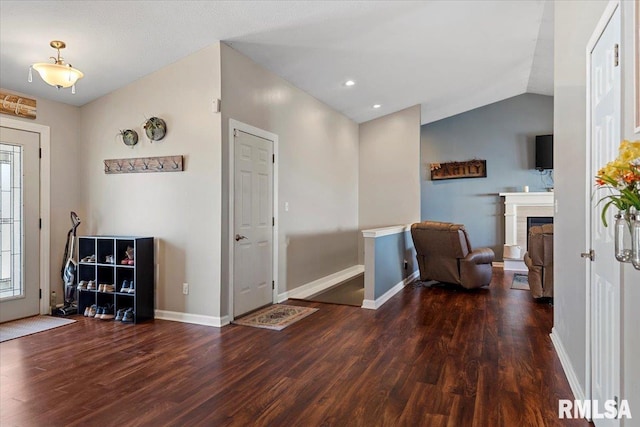 foyer entrance with baseboards, lofted ceiling, wood finished floors, and a fireplace