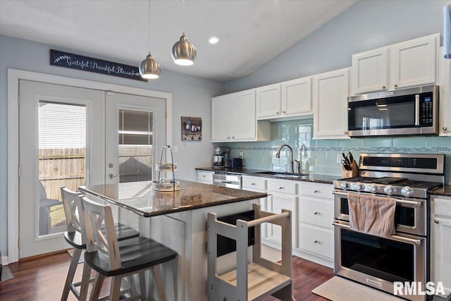 kitchen featuring a breakfast bar area, a sink, stainless steel appliances, vaulted ceiling, and french doors