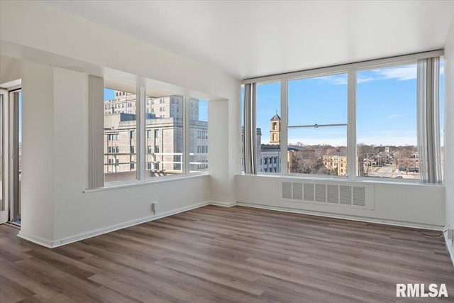 empty room featuring visible vents, baseboards, a city view, and wood finished floors