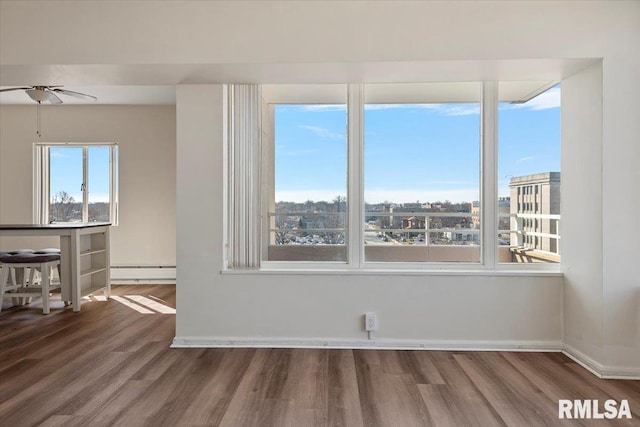 unfurnished room with a ceiling fan, wood finished floors, baseboards, a baseboard radiator, and a view of city