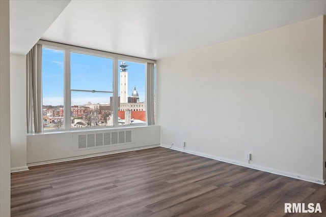 empty room with a city view, wood finished floors, visible vents, and baseboards