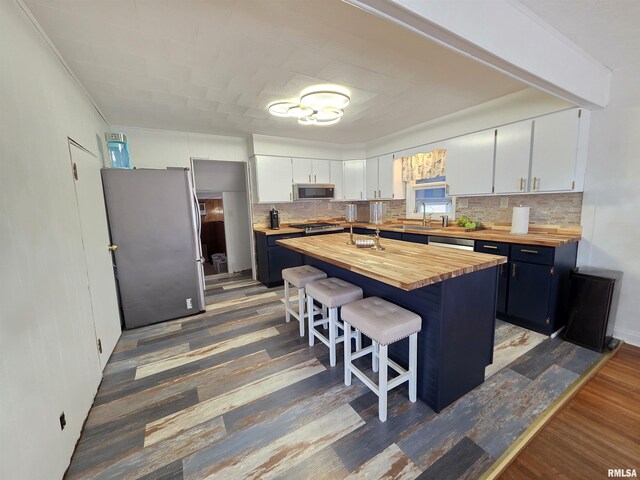 kitchen with wood finished floors, wooden counters, appliances with stainless steel finishes, a kitchen bar, and backsplash