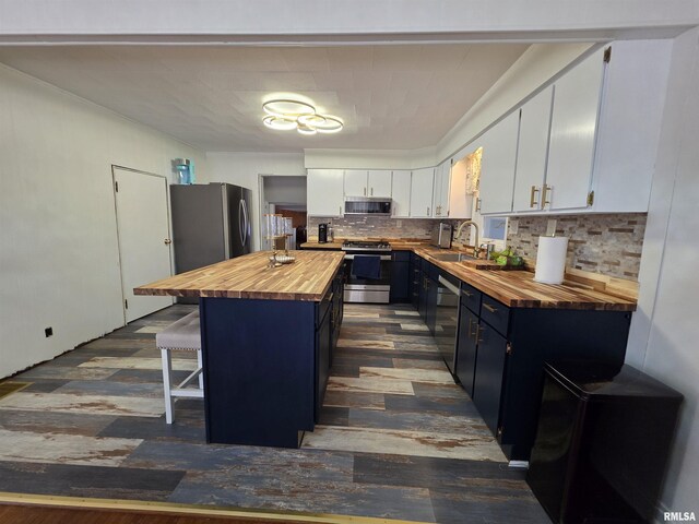 kitchen featuring wooden counters, blue cabinetry, a sink, appliances with stainless steel finishes, and a kitchen bar