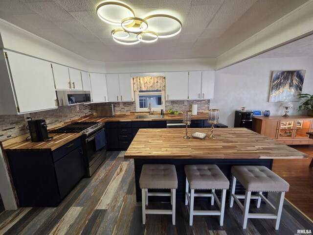 kitchen featuring a breakfast bar area, decorative backsplash, white cabinets, appliances with stainless steel finishes, and butcher block counters