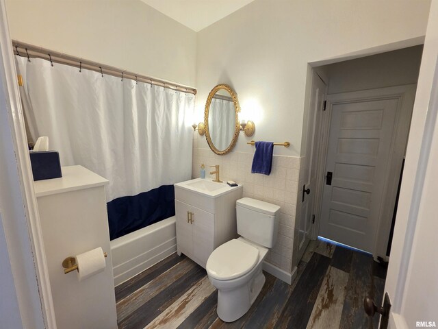 bathroom with wood finished floors, shower / bath combo with shower curtain, wainscoting, tile walls, and toilet