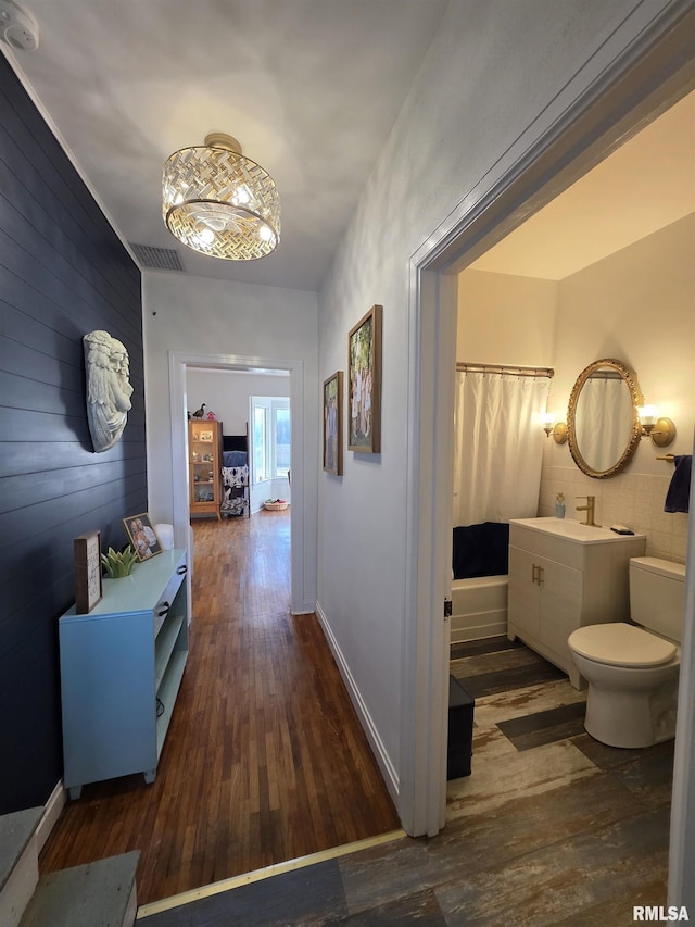 corridor featuring a sink, visible vents, baseboards, and dark wood-style flooring