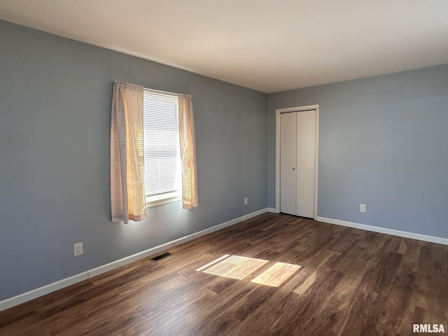 spare room featuring dark wood-style floors, visible vents, and baseboards