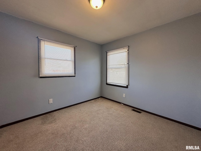 empty room featuring plenty of natural light, light colored carpet, visible vents, and baseboards