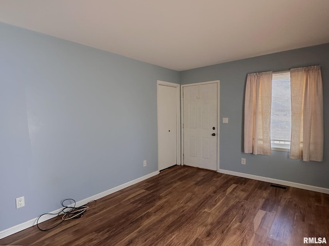 empty room featuring visible vents, baseboards, and dark wood finished floors